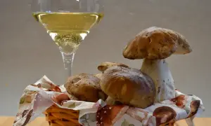 Un bicchiere di vino frizzante, perfetto vino da abbinare ai funghi porcini appena raccolti in un cestino.