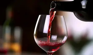 Versando un bicchiere di Carmignano vino rosso, con riflessi luminosi e una bottiglia scura sullo sfondo.