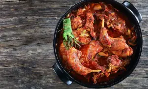Un saporito coniglio al vino rosso, cotto lentamente con erbe aromatiche, in una casseruola nera su un tavolo di legno rustico.