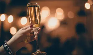 Mano con smalto rosso tiene un calice di champagne extra dry, con luci sfocate sullo sfondo.