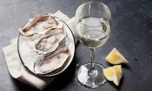 Piatto di ostriche fresche su ghiaccio, accompagnato da un bicchiere di vino francese per ostriche e spicchi di limone.