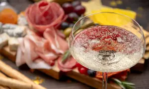 Un bicchiere di spumanti italiani famosi, con un tagliere di salumi, formaggi e uva sullo sfondo.