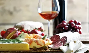 Tagliere con salumi, formaggi, uva e pane. Un bicchiere di vino rosato suggerisce perfetti vermentino abbinamenti.