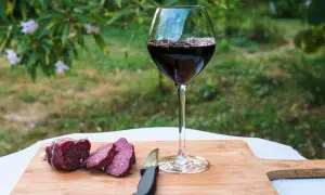 Un bicchiere di vino rosso e salumi affettati su un tagliere di legno, perfetti per le associazioni vini e salumi naturali.