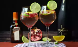 Due calici di sangria con prosecco, guarniti con lime e melograno, accanto a bottiglie di Cointreau e Freixenet.