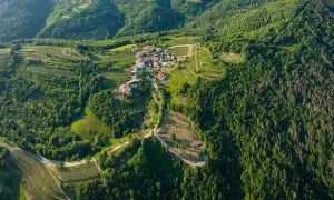 Un borgo pittoresco nel **Collio Goriziano**, immerso tra vigneti terrazzati e boschi lussureggianti, con case dai tetti rossi che si aggrappano alle dolci colline.