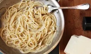 Spaghetti cacio e pepe cremosi, pronti per un perfetto abbinamento vino. Pepe macinato fresco e pecorino a lato.