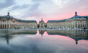 Piazza specchiata al tramonto, con edifici eleganti che ricordano il fascino del Medoc Bordeaux.