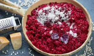 Risotto rosso vibrante, guarnito con parmigiano grattugiato e basilico. Accanto, ingredienti per un perfetto vino rosso per risotto.