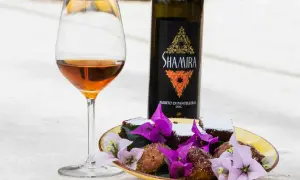 Calice di passito di Pantelleria accanto a dolcetti e fiori viola.