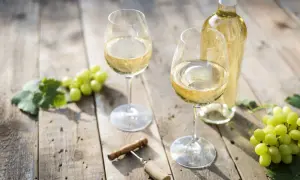 Due calici di vino bianco, una bottiglia, uva e cavatappi su un tavolo di legno. Le caratteristiche del Pouilly-Fumé si riflettono in questo scenario.