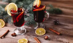 Due bicchieri di vino per vin brulé, decorati con fette d'arancia e cannella, su un tavolo di legno con rami di pino.