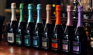 Una fila di bottiglie di Prosecco Serena, ognuna con un tappo colorato. Il brut è un Prosecco, perfetto per ogni occasione.