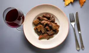 Piatto di cinghiale in umido con un bicchiere di vino rosso, perfetto vino da abbinare al cinghiale.