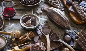 Un bicchiere di vino rosso accompagna una ricca selezione di cioccolato, dai chicchi di cacao alle tavolette, per un'esperienza golosa.
