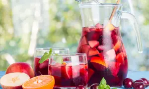 Caraffa e bicchieri pieni di sangria, con frutta fresca come mele, arance e ciliegie. Perfetta per fare la sangria in una giornata estiva.