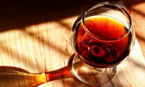 Un bicchiere di **marsala vino** ambrato riposa su un tavolo di legno, illuminato da raggi di sole che creano ombre suggestive.