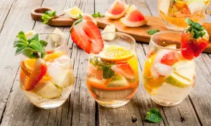Tre bicchieri di sangria con vino bianco, fragole, arance, mele e menta su un tavolo di legno.