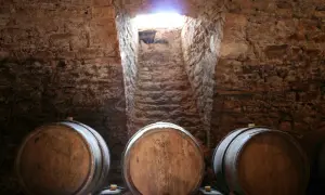 Cantine in pietra con botti di legno, un raggio di luce illumina la scala. Un'atmosfera che evoca il **Rodano, Francia**, e i suoi vini pregiati.