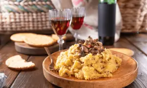 Polenta con funghi, perfetta con un buon vino da abbinare alla polenta. Due calici rossi e una bottiglia completano la scena rustica.