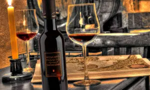 Una bottiglia e un calice di Moscato di Scanzo, illuminati da una candela, su un tavolo con una mappa antica.