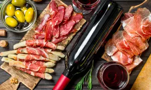 Un bicchiere e una bottiglia di vino rosso bordeaux, accompagnati da salumi, grissini, olive e noci, creano un'atmosfera conviviale.