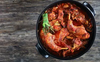 Un saporito coniglio al vino rosso, cotto lentamente con erbe aromatiche, in una casseruola nera su un tavolo di legno rustico.