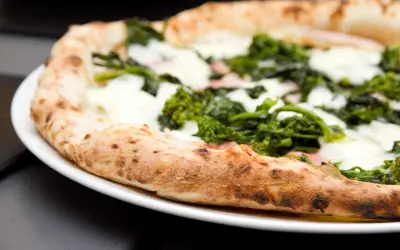Pizza con verdure e mozzarella su un piatto bianco, un'ottima scelta per una serata con pizza e champagne.