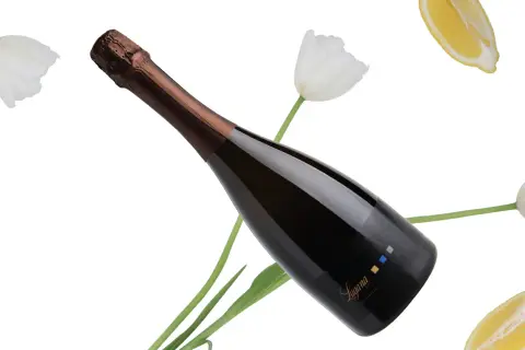 Bottiglia di spumante Trebbiano di Lugana tra tulipani bianchi e fette di limone, con un'etichetta che riporta il nome "Lugana".