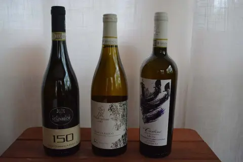 Tre bottiglie di vino bianco, tra cui un Lison Classico di Pramaggiore, su un tavolo di legno.