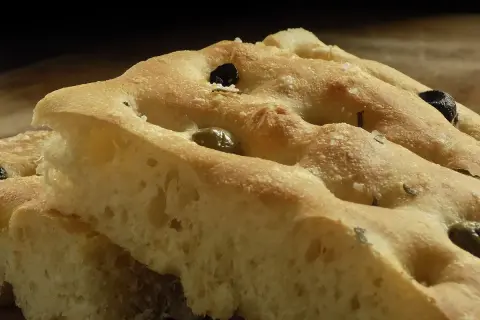 Focaccia soffice con olive e rosmarino, perfetta da gustare con un buon vino.