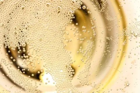 Bollicine dorate salgono in un bicchiere, evocando la freschezza di un Franciacorta Prosecco.