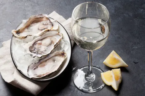Piatto di ostriche fresche su ghiaccio, accompagnato da un bicchiere di vino francese per ostriche e spicchi di limone.