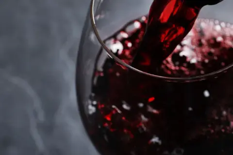 Versando vino rosso rubino in un calice, evocando i sapori autentici dei vini lucani.