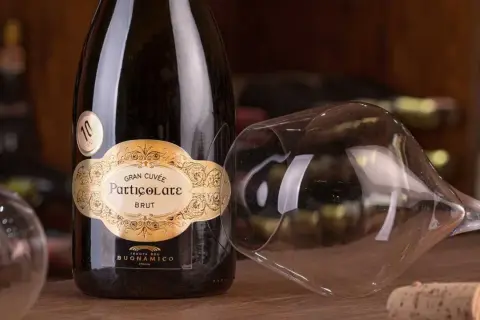 Bottiglia di spumante Gran Cuvée Particolare Brut, con calice rovesciato e tappo di sughero. Il "brut" indica la secchezza del vino.