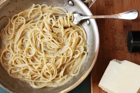 Spaghetti cacio e pepe cremosi, pronti per un perfetto abbinamento vino. Pepe macinato fresco e pecorino a lato.