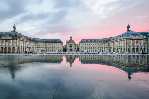 Piazza specchiata al tramonto, con edifici eleganti che ricordano il fascino del Medoc Bordeaux.