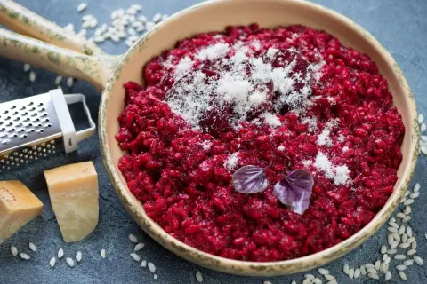 Risotto rosso vibrante, guarnito con parmigiano grattugiato e basilico. Accanto, ingredienti per un perfetto vino rosso per risotto.
