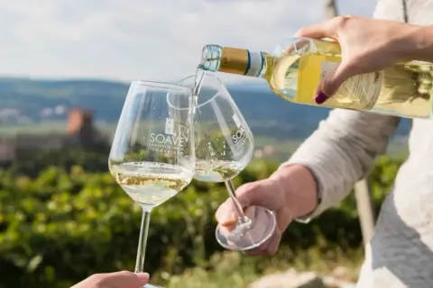 Versando soave wine in due calici con sfondo di vigneti e castello.