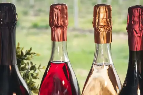Quattro bottiglie di vini più pregiati, con tappi color rame, oro e rosso, pronte per essere degustate.