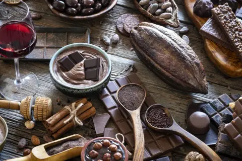 Un bicchiere di vino rosso accompagna una ricca selezione di cioccolato, dai chicchi di cacao alle tavolette, per un'esperienza golosa.