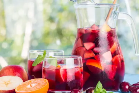 Caraffa e bicchieri pieni di sangria, con frutta fresca come mele, arance e ciliegie. Perfetta per fare la sangria in una giornata estiva.