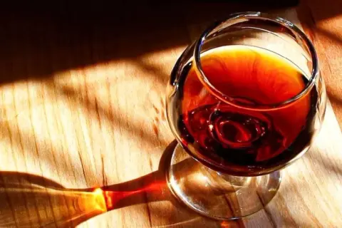 Un bicchiere di **marsala vino** ambrato riposa su un tavolo di legno, illuminato da raggi di sole che creano ombre suggestive.