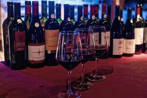 Degustazione di vini rossi, tra cui Teroldego Rotaliano, provenienti dal Trentino Alto Adige. Le bottiglie sono allineate, con tre calici pieni in primo piano.