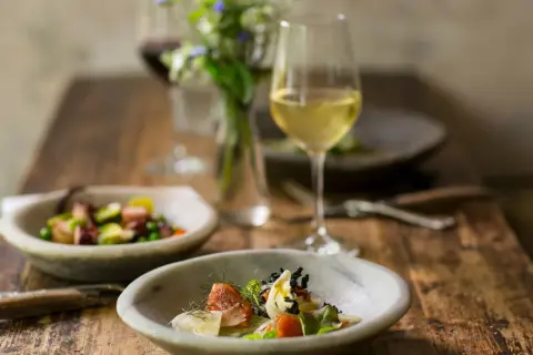 Deliziosi piatti con pesce e verdure, perfetti per i pinot grigio abbinamenti. Un bicchiere di vino bianco attende accanto a un bouquet di fiori.
