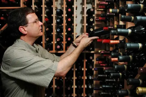 Uomo in cantina sceglie tra bottiglie di vino, tra cui uve cabernet.