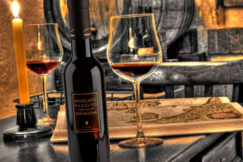 Una bottiglia e un calice di Moscato di Scanzo, illuminati da una candela, su un tavolo con una mappa antica.