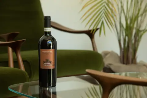 Bottiglia di vino umbro famoso, Poggio Miniera, su un tavolino di vetro, con poltrone verdi e una pianta sullo sfondo.
