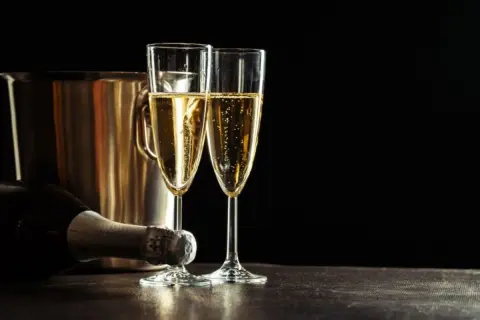 Due calici di champagne scintillante, una bottiglia e un secchiello per il ghiaccio. Un'uva per lo champagne, pronta per essere gustata.