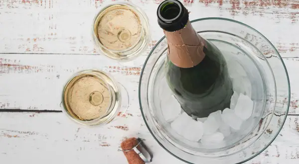 Due bicchieri di Prosecco e una bottiglia in un secchiello di ghiaccio. La temperatura ideale per il Prosecco è tra 6-8 gradi.